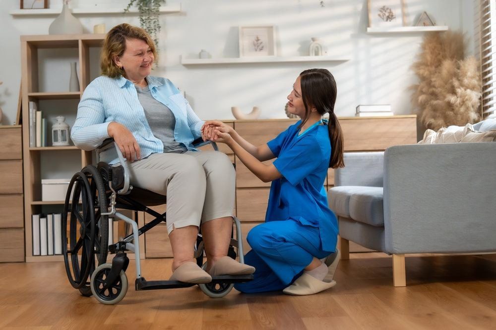 A nurse kneeling and holding hands with a woman in a wheelchair, sharing a warm moment.