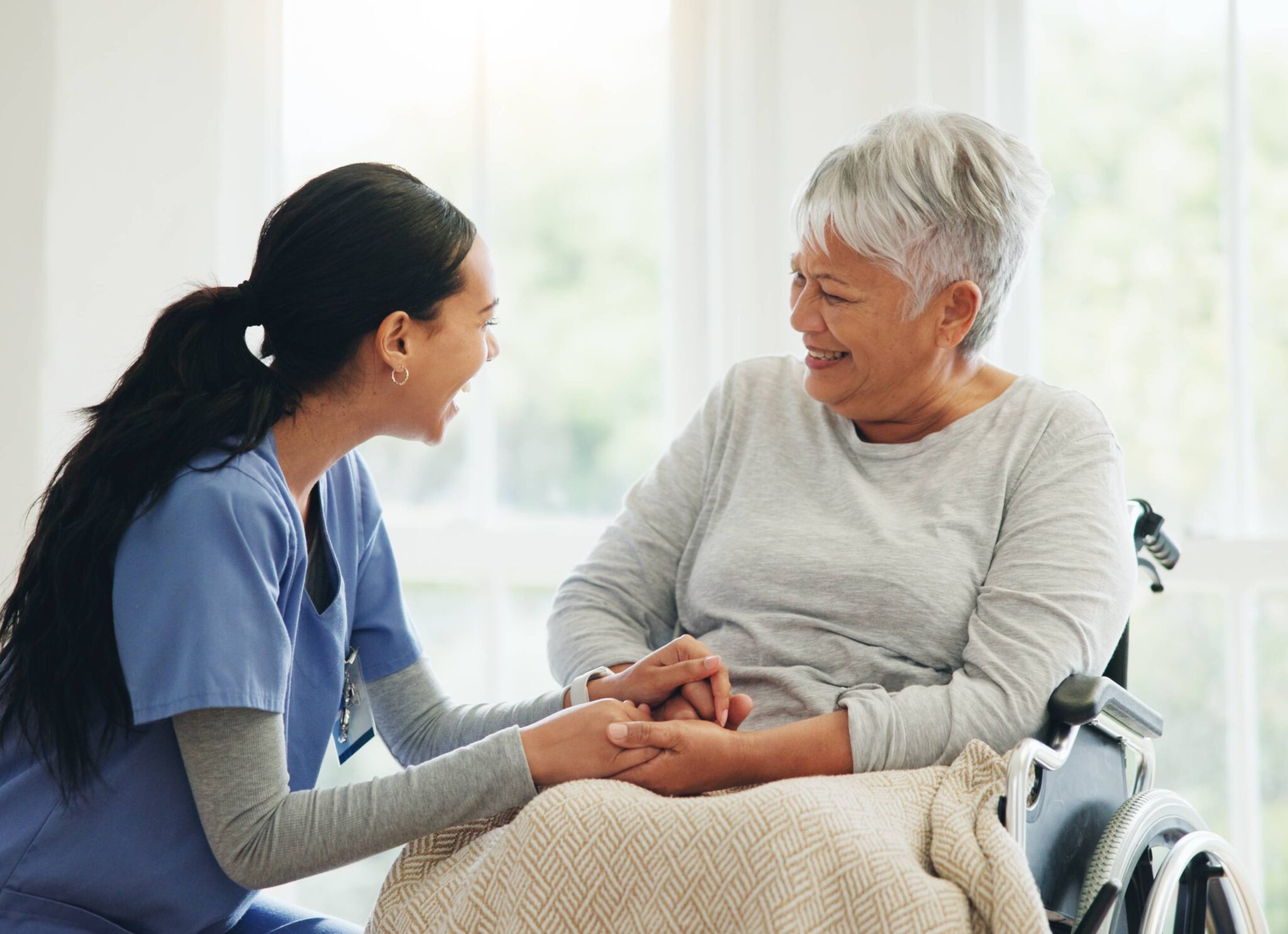 A nurse warmly holding hands with an elderly woman in a wheelchair.