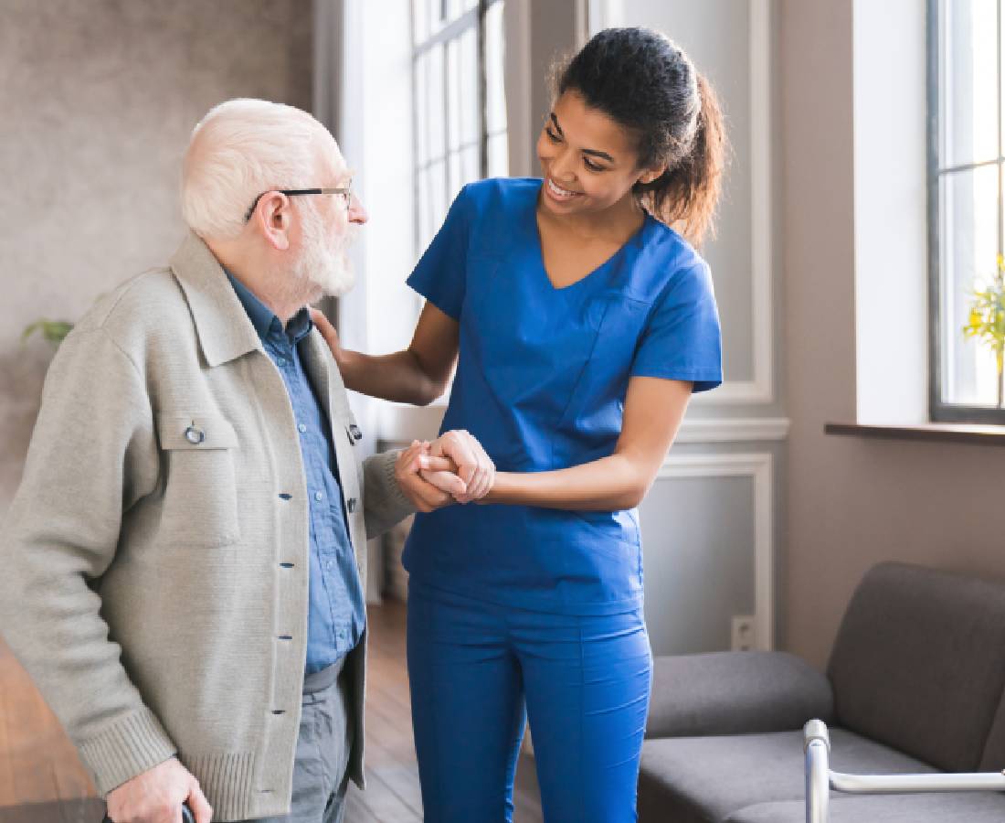 A nurse assisting an elderly man with walking indoors.
