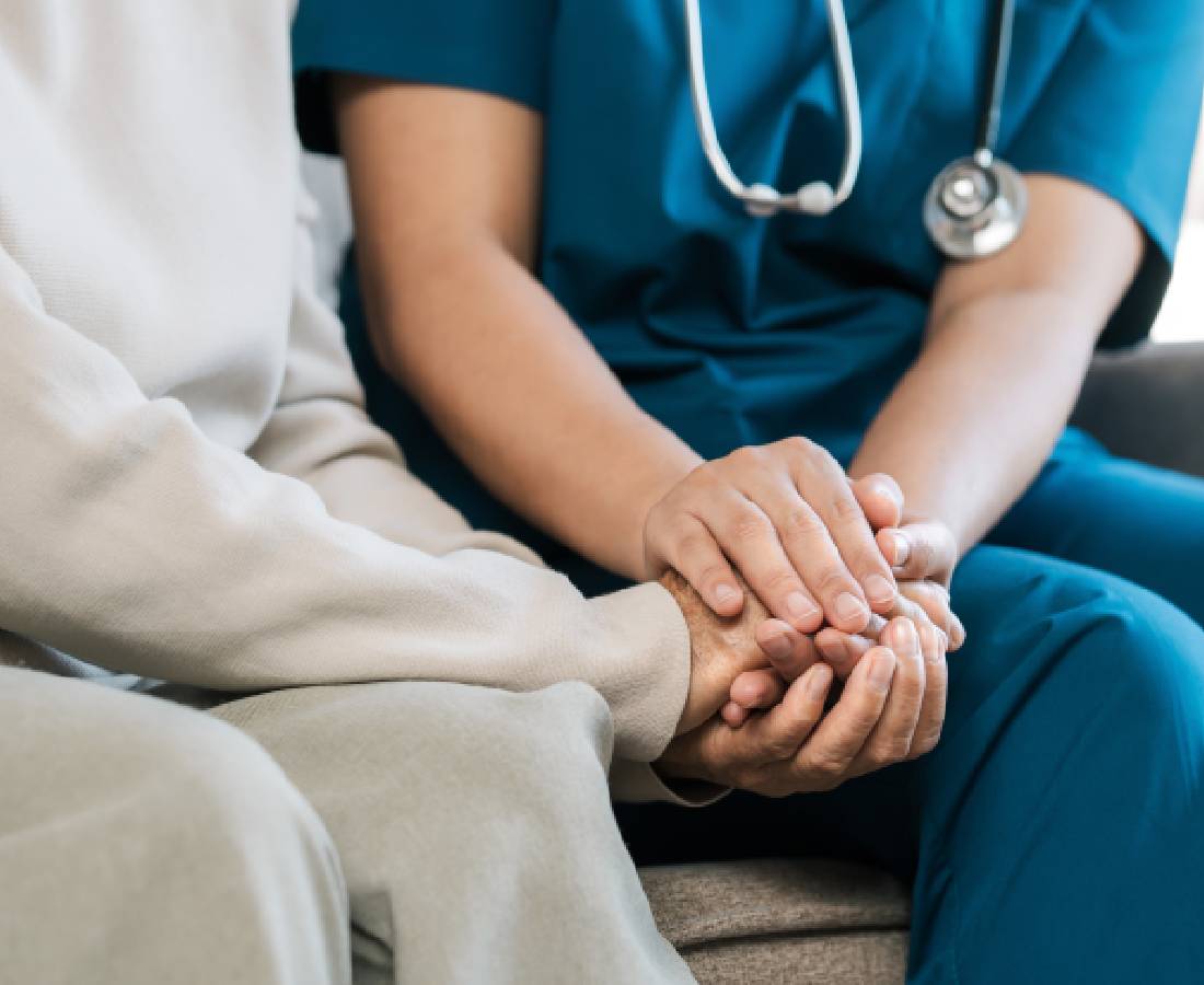 A healthcare worker comforting an elderly person by holding their hands.