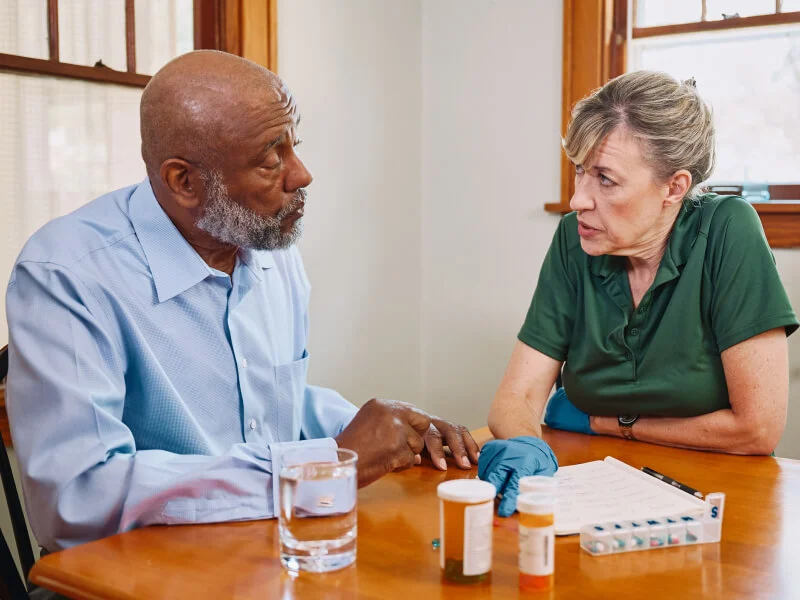 A senior man and woman discussing medication at a table.