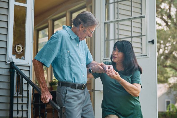 A woman helps an elderly man with his shirt button.