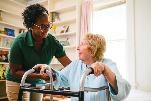 Caregiver assisting elderly woman with walker indoors.