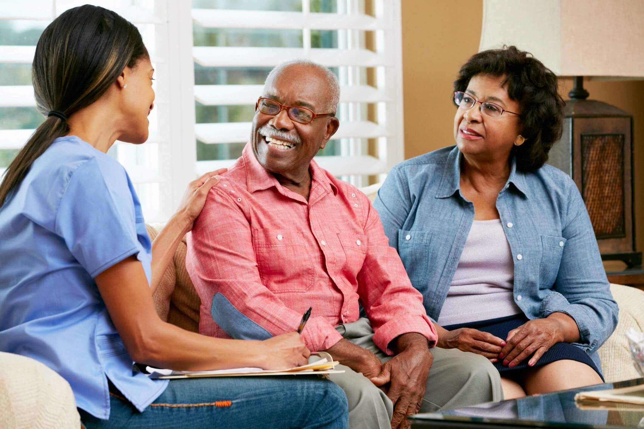 A caregiver talking with an elderly couple in a cozy setting.
