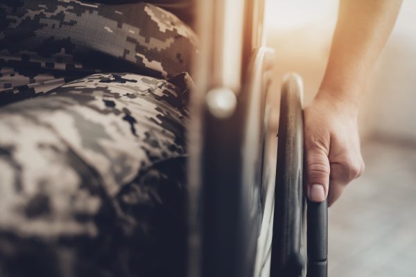 Close-up of a person in camouflage holding a wheelchair wheel.