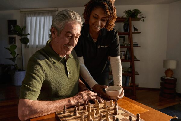 An elderly man and woman play chess together at a wooden table.