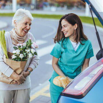 Nurse and elderly woman happily unloading groceries from car.