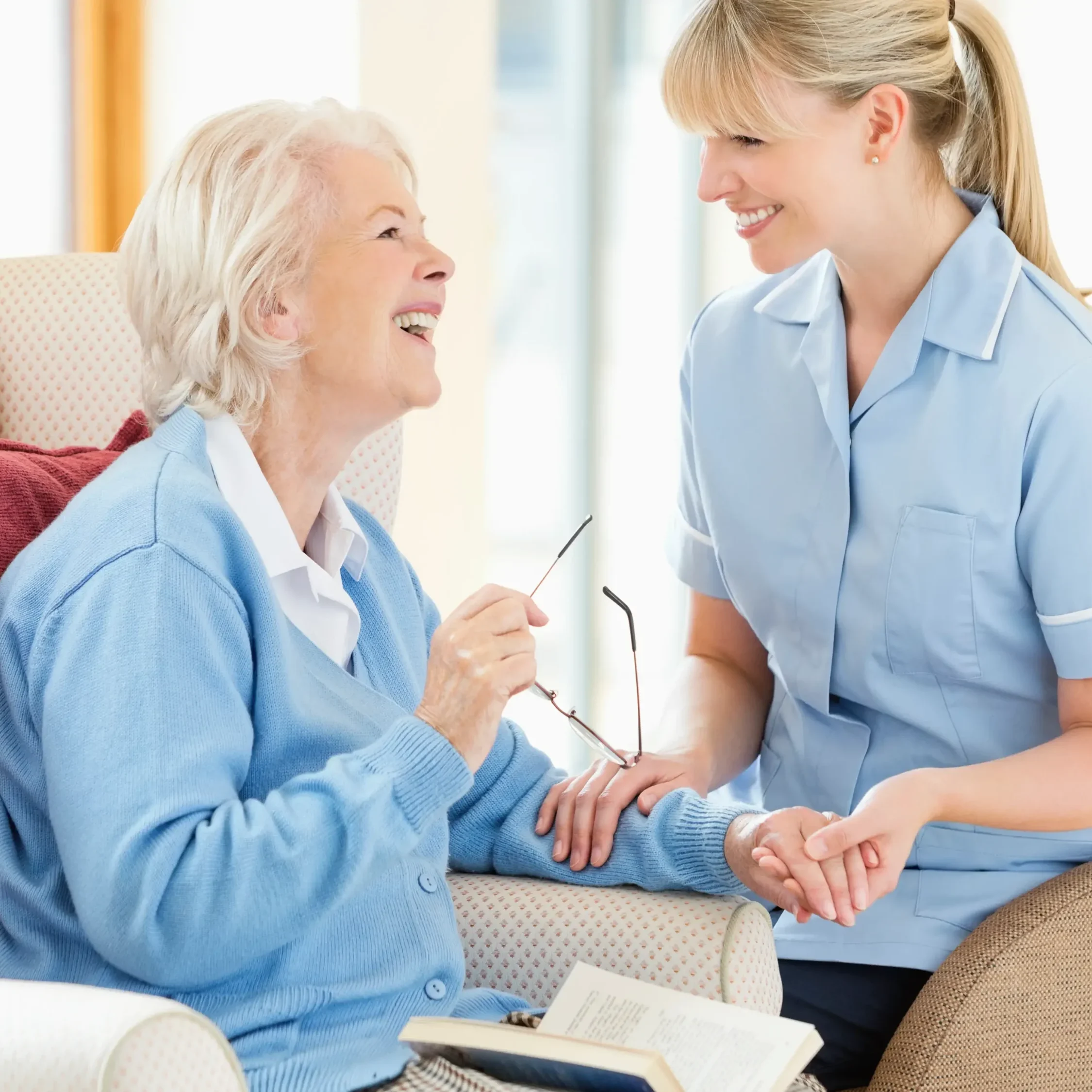 A caregiver smiling and holding hands with an elderly woman.