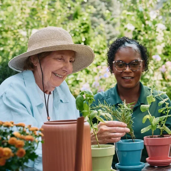 Two women gardening together outdoors with potted plants.