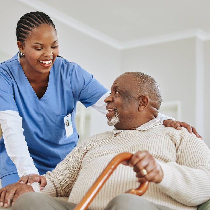 A nurse comforting an elderly man with a cane in a care setting.