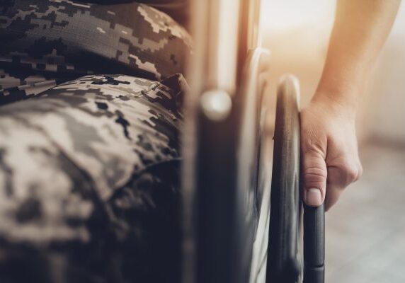 Close-up of a person in camouflage holding a wheelchair wheel.